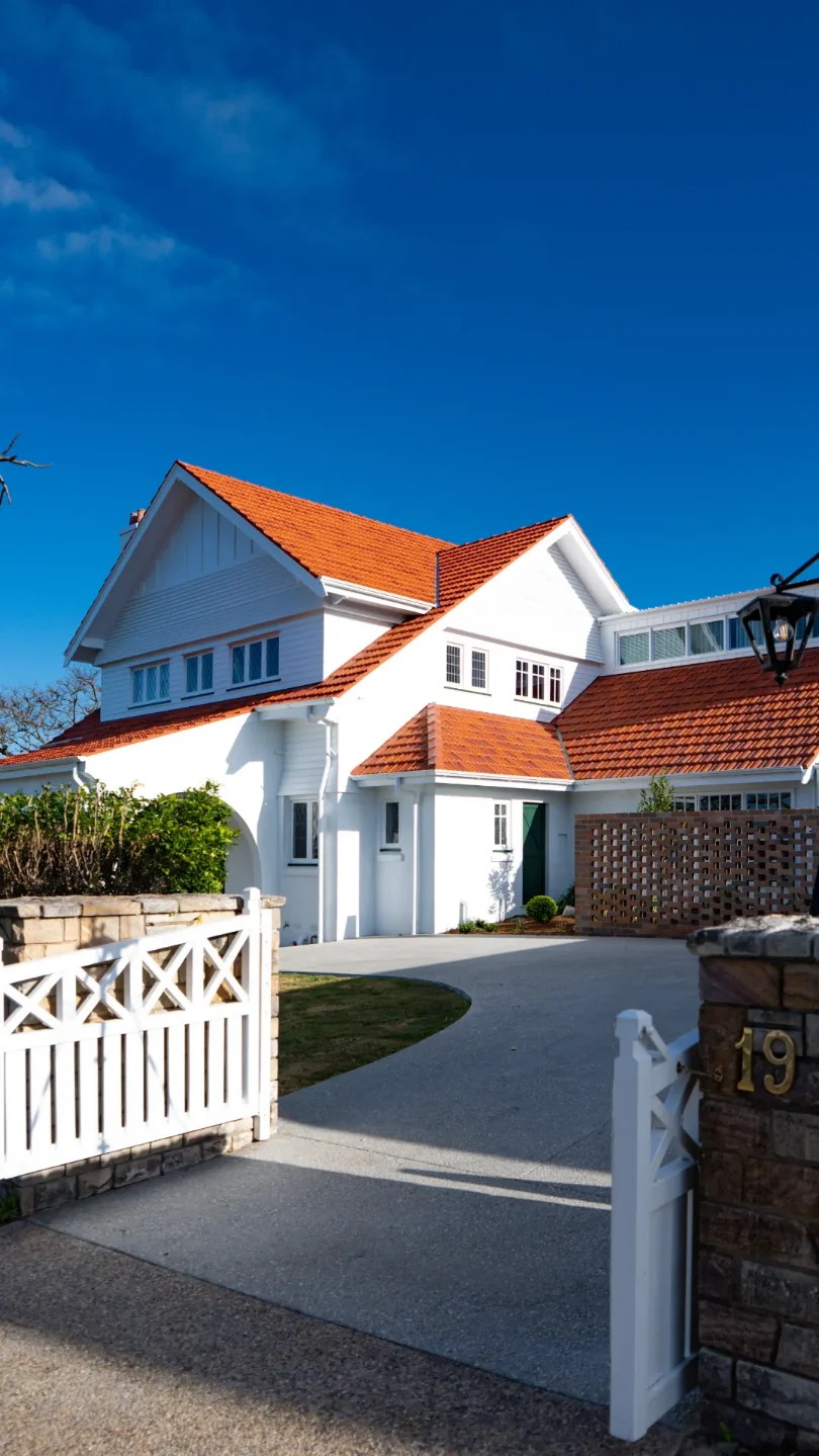 Two-storey white home with a terracotta tiled roof behind a white picket gate