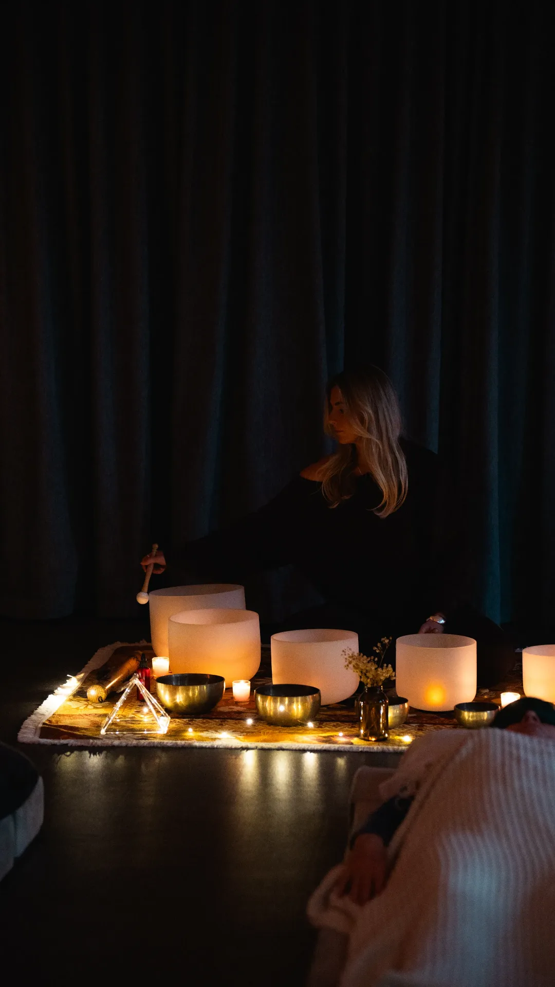 Practitioner playing crystal singing bowls by candlelight at a sound healing session